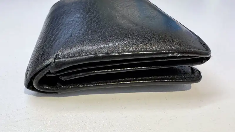 A black leather bifold wallet lying on a pale surface.