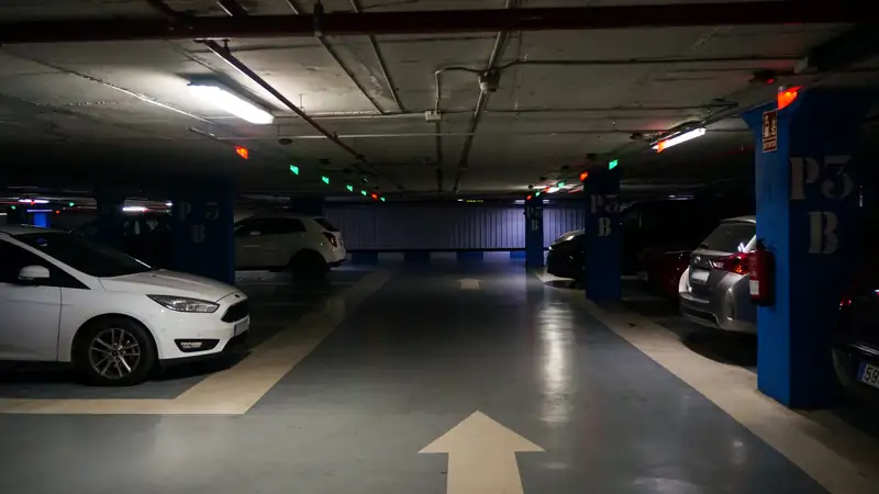 A dim underground parking garage with cars parked beside blue pillars and a painted arrow on the floor.