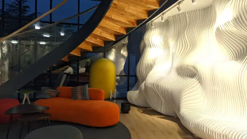 A modern office lounge with an orange sofa, a wooden staircase and a sculpted white wall.