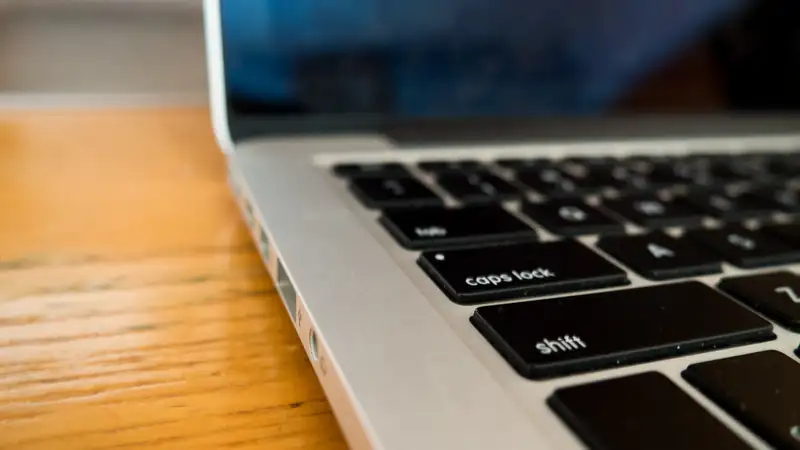 Close-up of a silver laptop keyboard resting on a warm wooden desk.