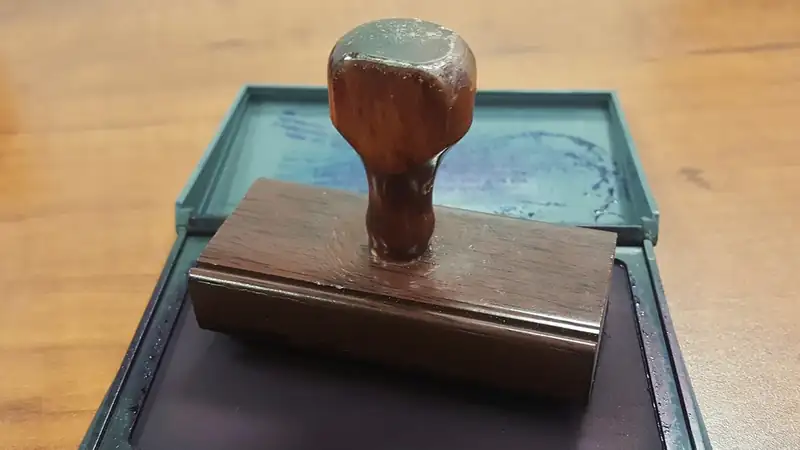 A wooden rubber stamp resting on an open ink pad on a wooden desk.